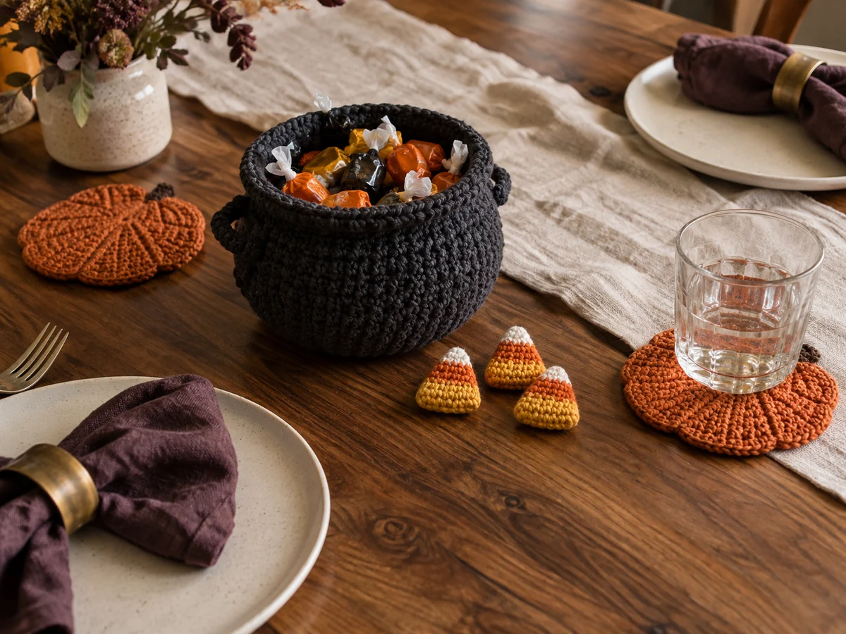 AI editorial Halloween table scene with a crochet cauldron of wrapped sweets, candy corn accents and pumpkin-shaped coasters on wood and linen.